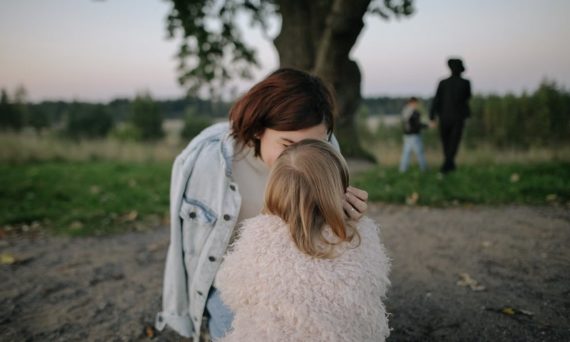 A tender moment between mother and daughter outdoors in a grassy field at twilight.