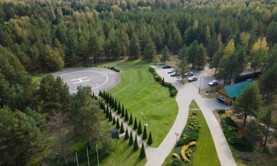 Aerial shot of a forest with a helipad, parking area, and landscaped gardens.